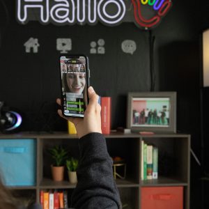 A hand holding a phone featuring the Hallo app in the Hallo office